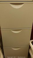 Front view of white Ikea file cabinet with three drawers and curved cut-out handles.