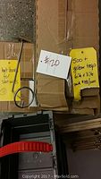 Photo showing yellow shipping tags and part of a metal hat display hanger with clamp for slat wall.