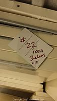 Stacked white IKEA STOLMEN shelf panels with handwritten tag indicating lot number and quantity