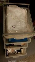 View of four clear plastic pull-out bins in IKEA Antonius plastic frame containing white tissue paper, envelopes, and miscellaneous office/packing supplies.