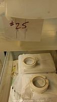 Close up of bin with packing tape rolls and white packing materials, with '#25' label on bin