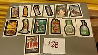 Top-down photo of 13 colorful Wacky Packages stickers laid out in rows on a flat surface, showing detailed humorous parodies of consumer products.