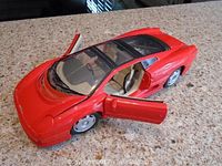 Red Jaguar XJ220 die-cast model with both doors open, showing tan interior and clear plastic roof, placed on granite counter.