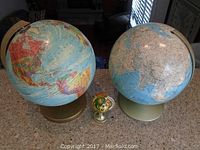 Photo of two large vintage globes and one small decorative globe item on countertop, showing overall lot contents.