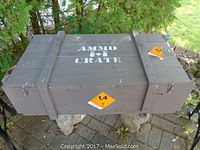 Exterior top view of wooden ammo crate showing 'AMMO CRATE' stenciled in white, orange hazard labels, and rope handles.