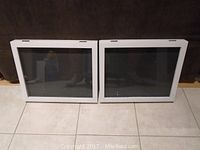 Photo of two white shadow boxes with glass fronts standing upright on the floor, positioned side by side showing front view