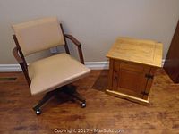 Pine end table next to retro office chair on hardwood floor against beige wall.