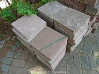 Stacked square concrete patio stones with reddish and grayish tones, showing heavy wear and outdoor use marks, approximately 12x12 inches each.