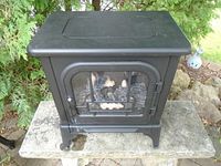 Front view of black Kenwood electric stove with glass door and decorative grid, showing artificial logs inside.