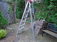 Full view of the aluminum step ladder standing in an outdoor patio area, showing the full frame and seven steps on each side.