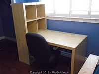 Overall view of IKEA shelf unit combined with desk and black office chair positioned near a window with white blinds.