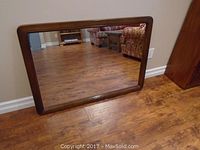 Front view of the retro large rectangular mirror with wood frame, showing the reflective surface and the wooden floor reflected in it.