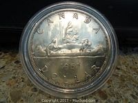Obverse side of the 1957 Canadian silver dollar showing a canoe with two paddlers, year 1957, and inscriptions 'CANADA DOLLAR'. Coin held in a protective transparent case.