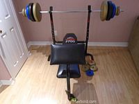 Full view of York 7700 bench with barbell and weights on a wooden floor against a wall