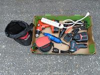Top-down photo showing all tools in a cardboard box including drills, rotary tool, sander, charger, and power strip.