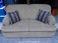 Front view of beige fabric sofa bed with two patterned square throw pillows.
