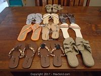 Nine pairs of women's sandals arranged on table, showing overall variety and styles in neutral and metallic tones.