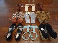 Nine pairs of women's sandals and shoes arranged on the floor, showing variety of styles and colors including brown, beige, silver, multi-color, tan, black, and blue.