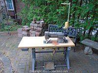 Overall view of machine mounted on wood table and metal stand with foot pedal below