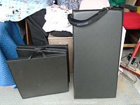 Two black rectangular fitness workout pads shown standing upright and leaning against fabric-covered furniture, one with a handle strap labeled Stott Pilates.