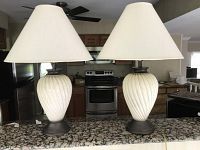 Pair of matching lamps on a granite countertop in front of a kitchen, showing white ceramic bases with ribbed spiral design and beige fabric shades.