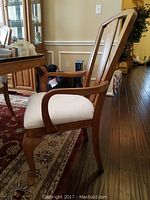 Side view of wooden arm dining chair showing curved armrests, cabriole legs, cream upholstered seat and vertical slats on backrest.