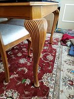 Close-up view showing the fluted, ornate carved leg detail of the oak dining table and one chair with white cushioned seat