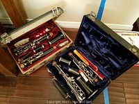 Two black clarinets disassembled and placed in their respective lined cases, showing overall wear and included accessories.