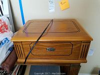 Front view of wooden Thomas Pacconi turntable with black decorative trim and attached power cord.