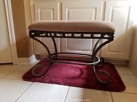 Front view of bench with metal scroll legs and cushioned beige fabric seat sitting on a red rug