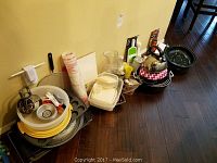 Wide view of the assortment of pots, pans, plastic containers, cups, and kitchen tools on the floor against a wall.