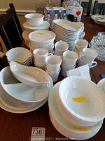 Multiple white dishes, bowls, and mugs arranged on a table, some with stickers showing quantity and price.