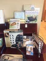 Full view of spa accessory items arranged including box of BackExpert2000, Kooshi soothing mat box, pillow protector packs, and foldable metal rack.