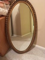 Full view of oval framed mirror standing upright on floor against wall.