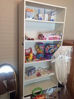 Full view of white 6-shelf bookcase with various toys and objects on shelves, showing overall condition and wear