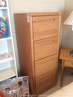 Full frontal view of a 4 drawer wooden filing cabinet showcasing its height and drawer design, placed beside a white shelf unit and wooden side table.