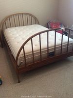Full view of the full size bed showing wood frame with curved headboard and footboard and mattress on top.