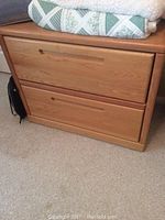 Front view of the wooden lateral filing cabinet showing two drawers with recessed handles, blankets and fabric on top.