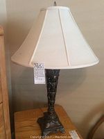 Full view of the lamp showing decorative metal base and white fabric shade on wooden table.