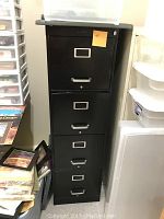 Black metal filing cabinet with four drawers and label holders on each drawer showing some signs of wear.