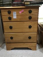 Full front view of the wooden bureau showing four drawers and dark metal handles. Some books are stacked on top.