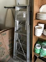 Two foldable aluminum ladders standing next to kitchen shelves and boxes.
