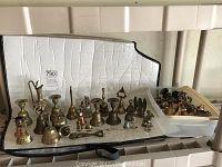 Overview of all brass bells, figurines, candle holders, and more arranged on a white cloth and plastic container with additional items.