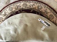 Rug fully visible from above showing its round shape and size estimation with minor spots and wear.