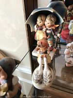 Figurine of two children under an umbrella with two geese, detailed front view