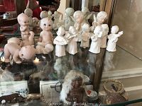 Front view of porcelain angel and child figurines displayed on glass shelf alongside small decorative vases and bowls.