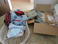 Folded vintage baby and toddler clothes in a wicker cradle and cardboard box, various pastel colors and fabrics