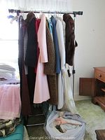 Photo of vintage coats, dresses, and bag of clothing on rack and floor
