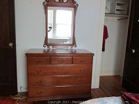 Front view of vintage wood dresser with brass handles and decorative mirror mounted above it.