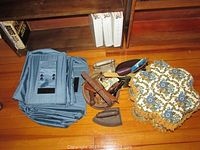 Photo showing blue collapsible hanging shoe caddy stacked beside basket of vintage sewing tools and two vintage cast irons on hardwood floor.